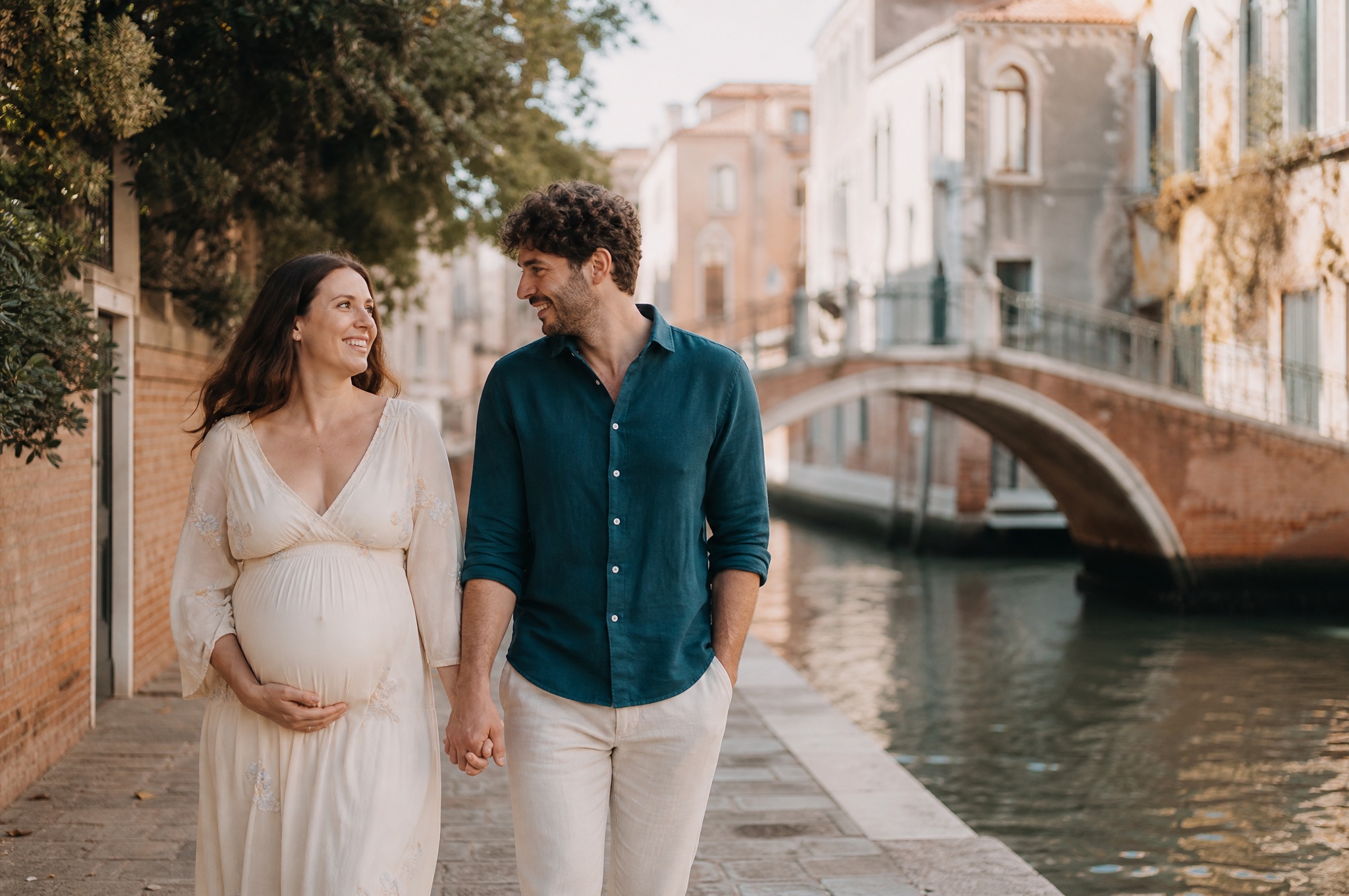 Expecting couple walking hand in hand along a quiet canal-side street in soft morning light